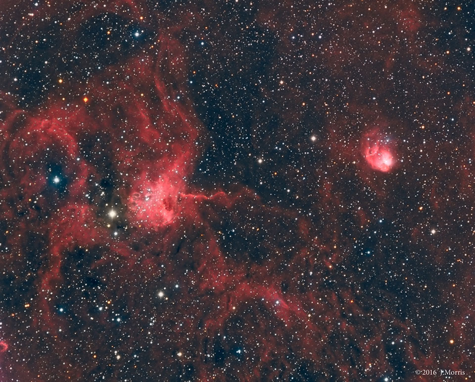 Zwei rote Nebel leuchten vor einem sternklaren Hintergrund, links ein größerer, der an eine Spinne erinnert, rechts ein kleiner runder - die Fliege.