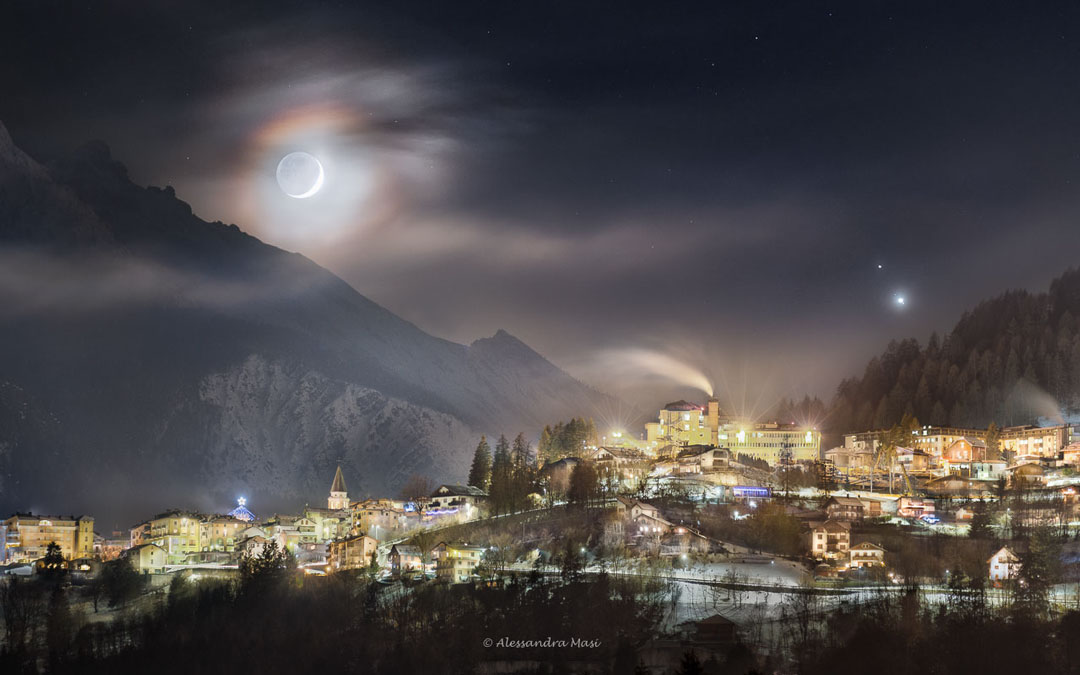 Mondkorona, Jupiter und Saturn über dem italienischen Dorf Pieve di Cadore und dem Sfornioi, der zur Bosconerogruppe gehört.