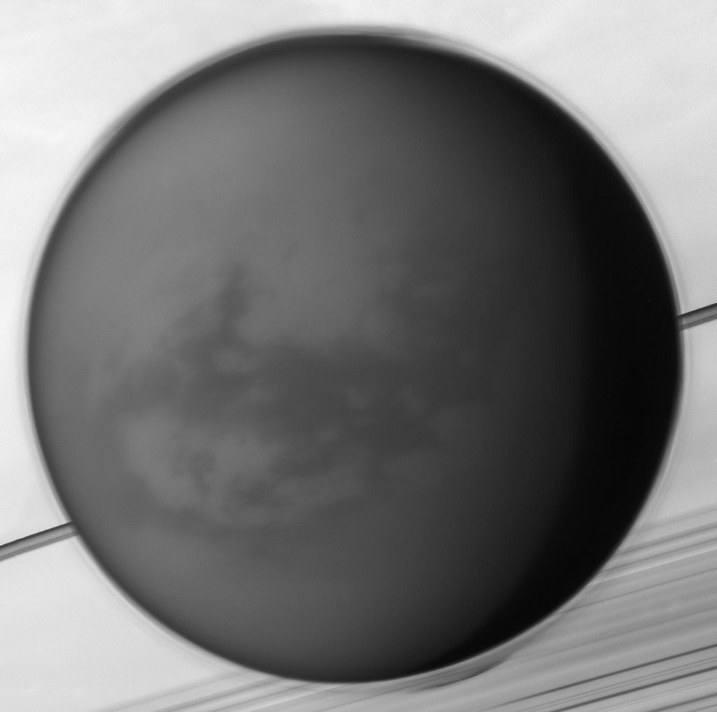 Die Raumsonde Cassini zeigt den Saturnmond Titan vor dem Gasriesenplaneten Saturn mit der dunklen, von Dünen bedeckten Region Shangri-La.