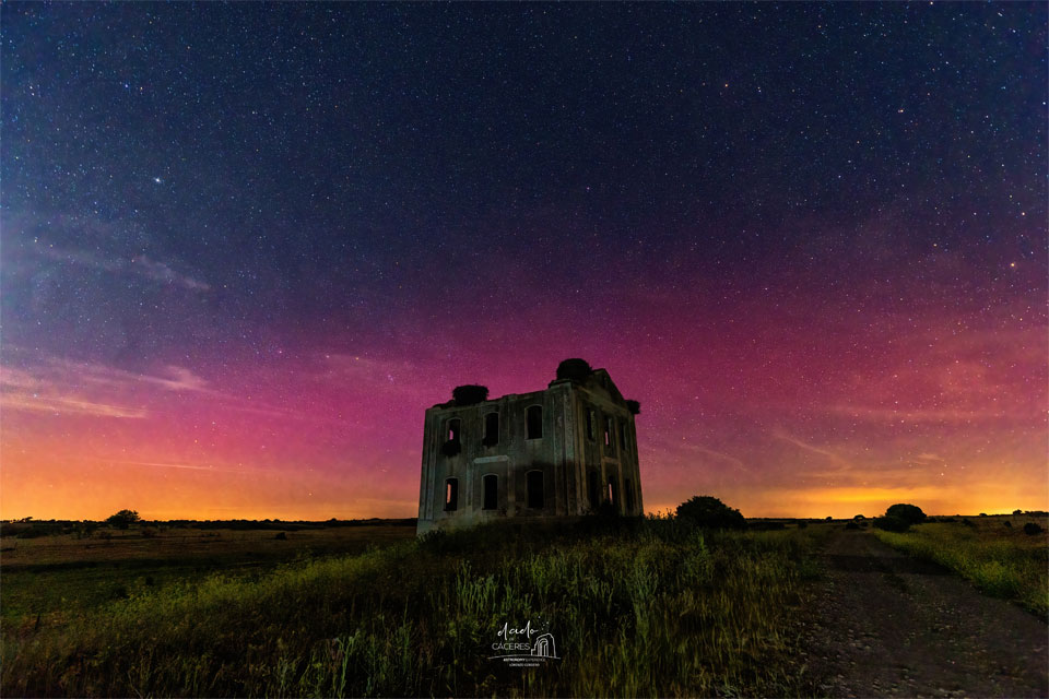 Über Cáceres in Zentralspanien leuchteten Polarlichter. Im Vordergrund ragt ein Gebäude über den Horizont, dahinter leuchtet der Himmel unten orangefarben und darüber violett.