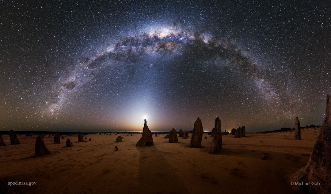 Über einer Landschaft mit spitzen Felstürmchen breitet sich ein Nachthimmel aus. Das Band der Milchstraße wölbt sich oben. Hell schimmerndes Zodiakallicht verbindet die Landschaft mit dem Himmel.