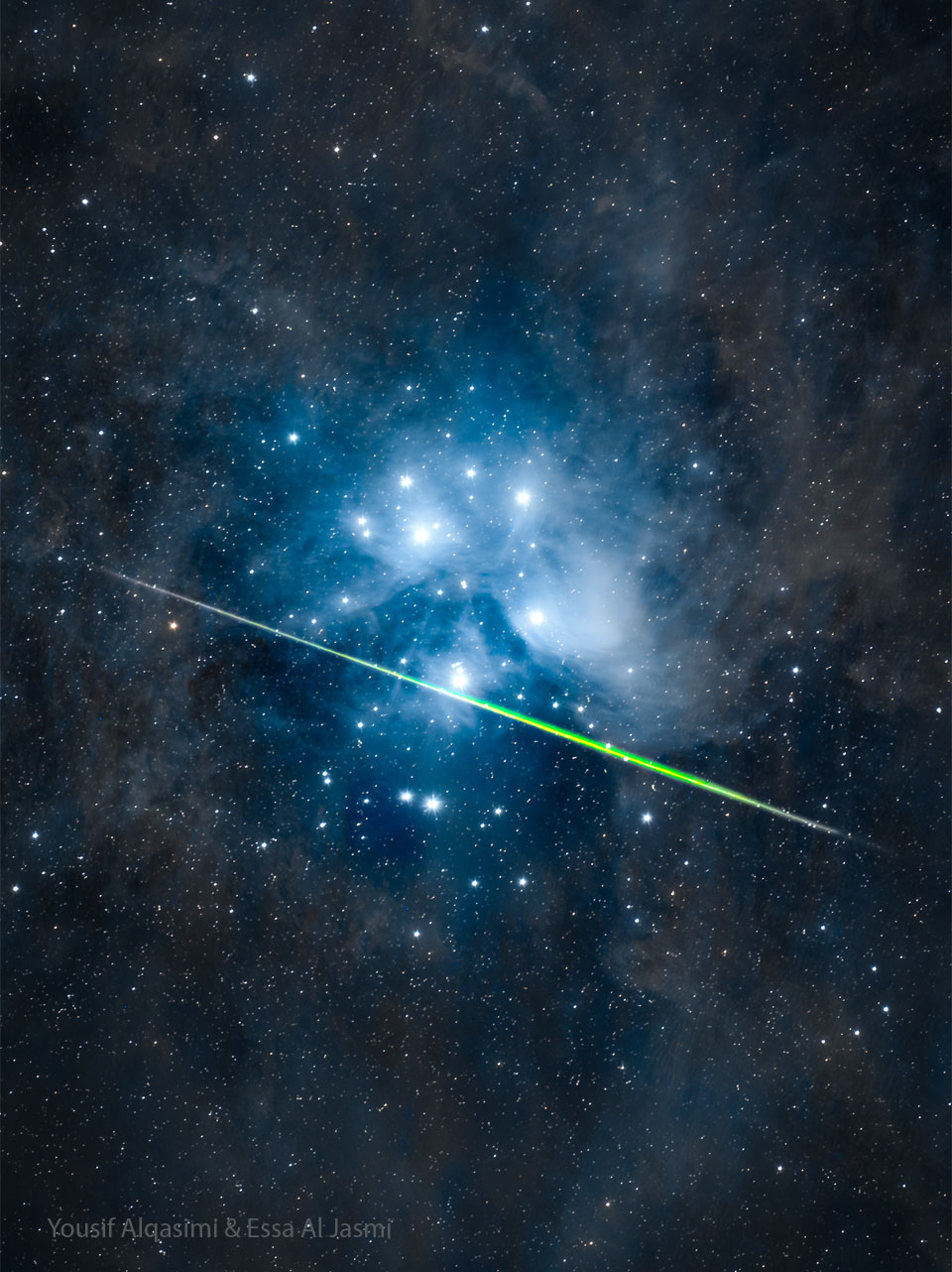 Vor den blau leuchtenden Nebeln der Plejaden zischt ein grüner Meteor vorbei.